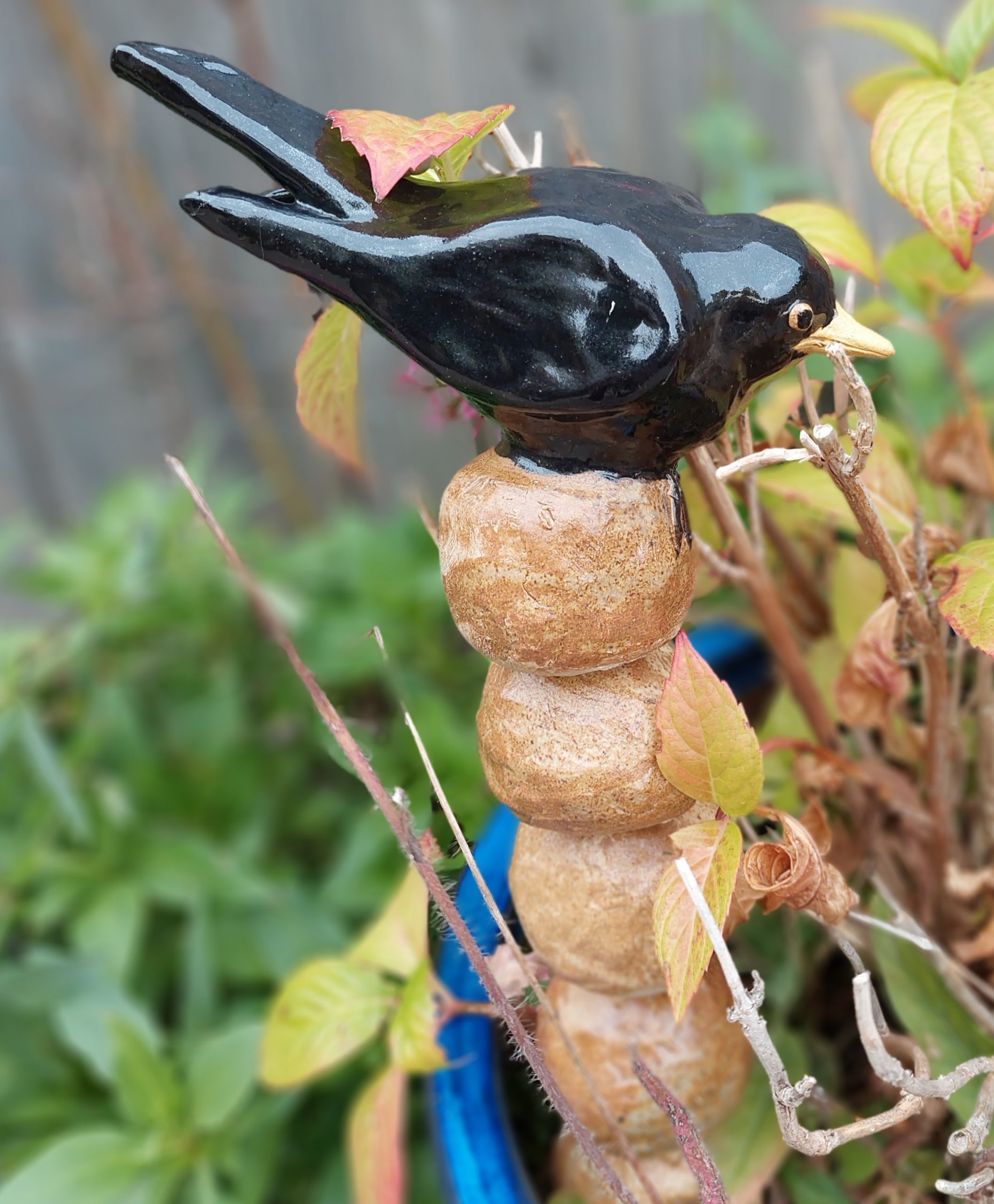 A decorative hand built stoneware blackbird on round stacking stones on a metal rod, placed in a plant pot.