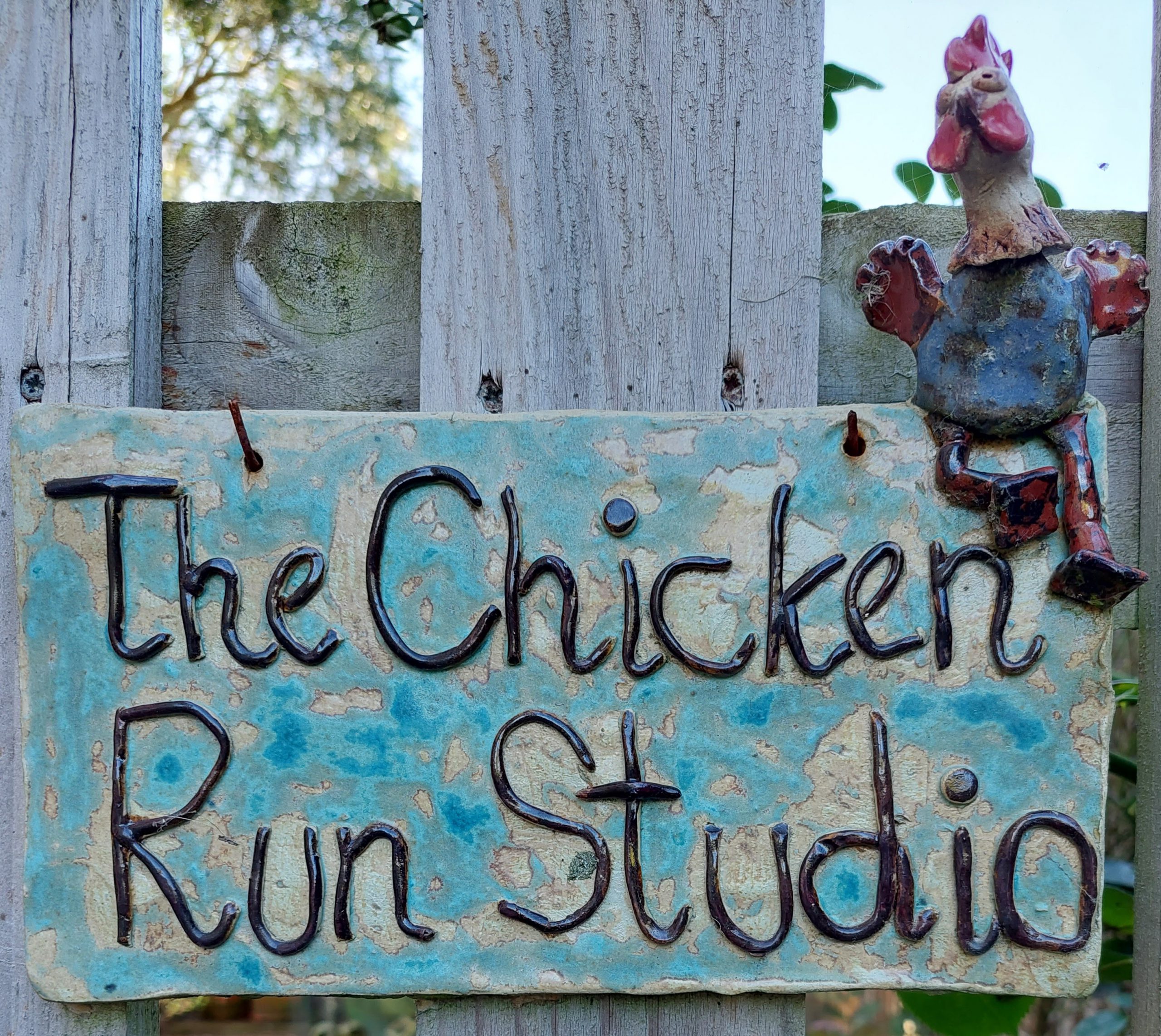 The Chicken Run Studio sign, made out of stoneware pottery, with a quirky stoneware chicken perched on the top.