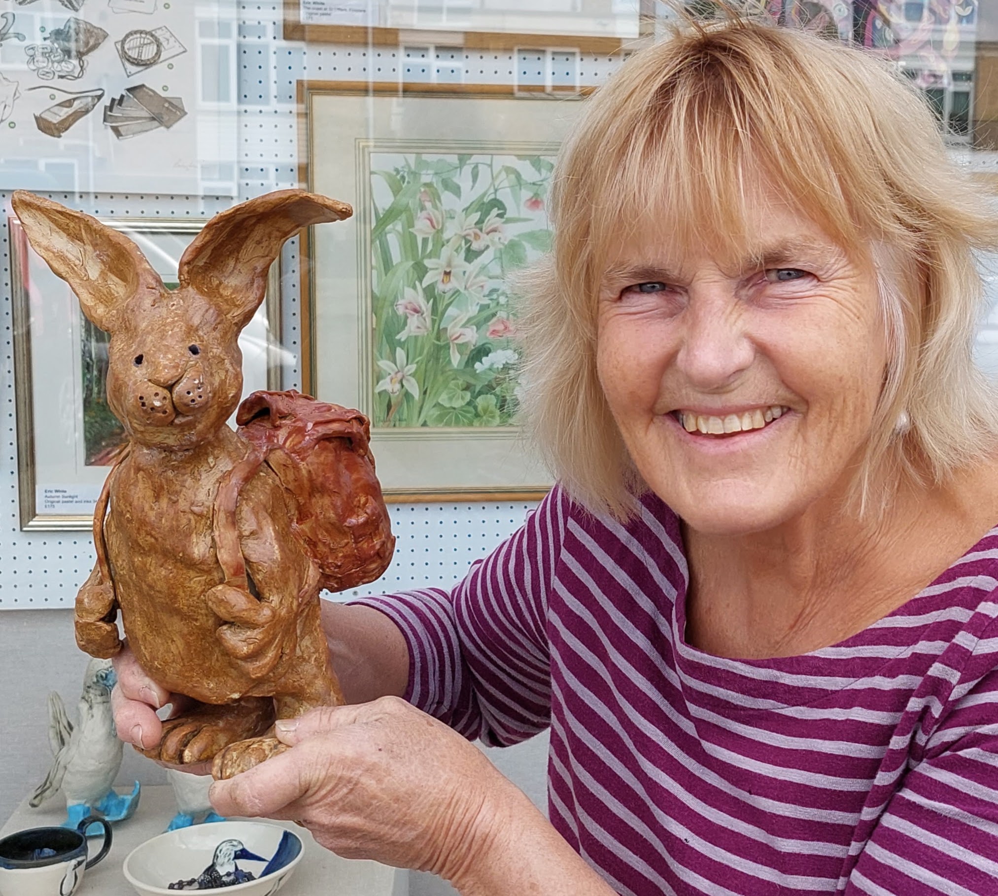 Potter Alison Holmans of The Chicken Run Studio holding a hand built quirky stoneware hare with a rucksack.